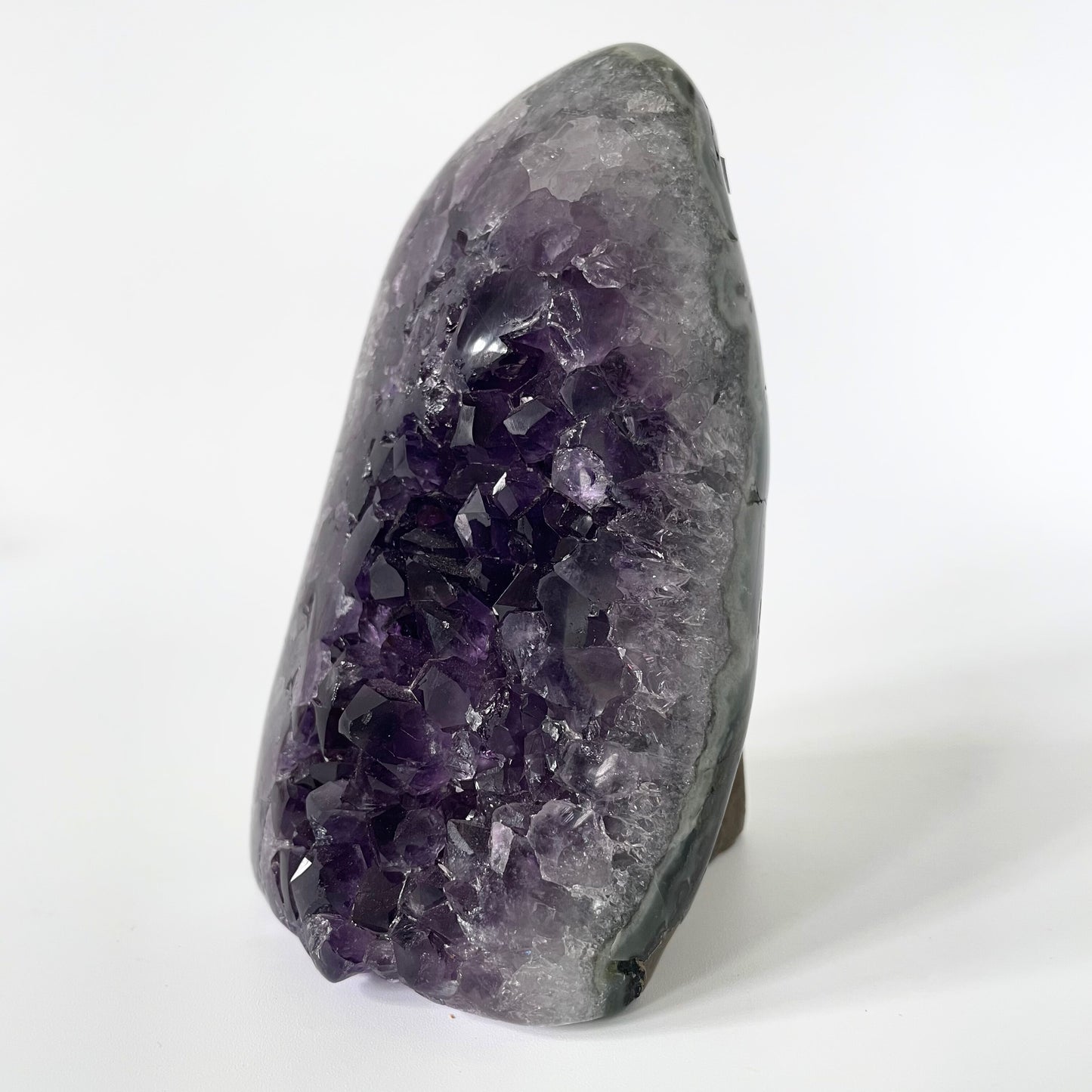 Amethyst cluster with polished edges and brilliant hues of deep purple and various sizes of crystal formations on a white background.