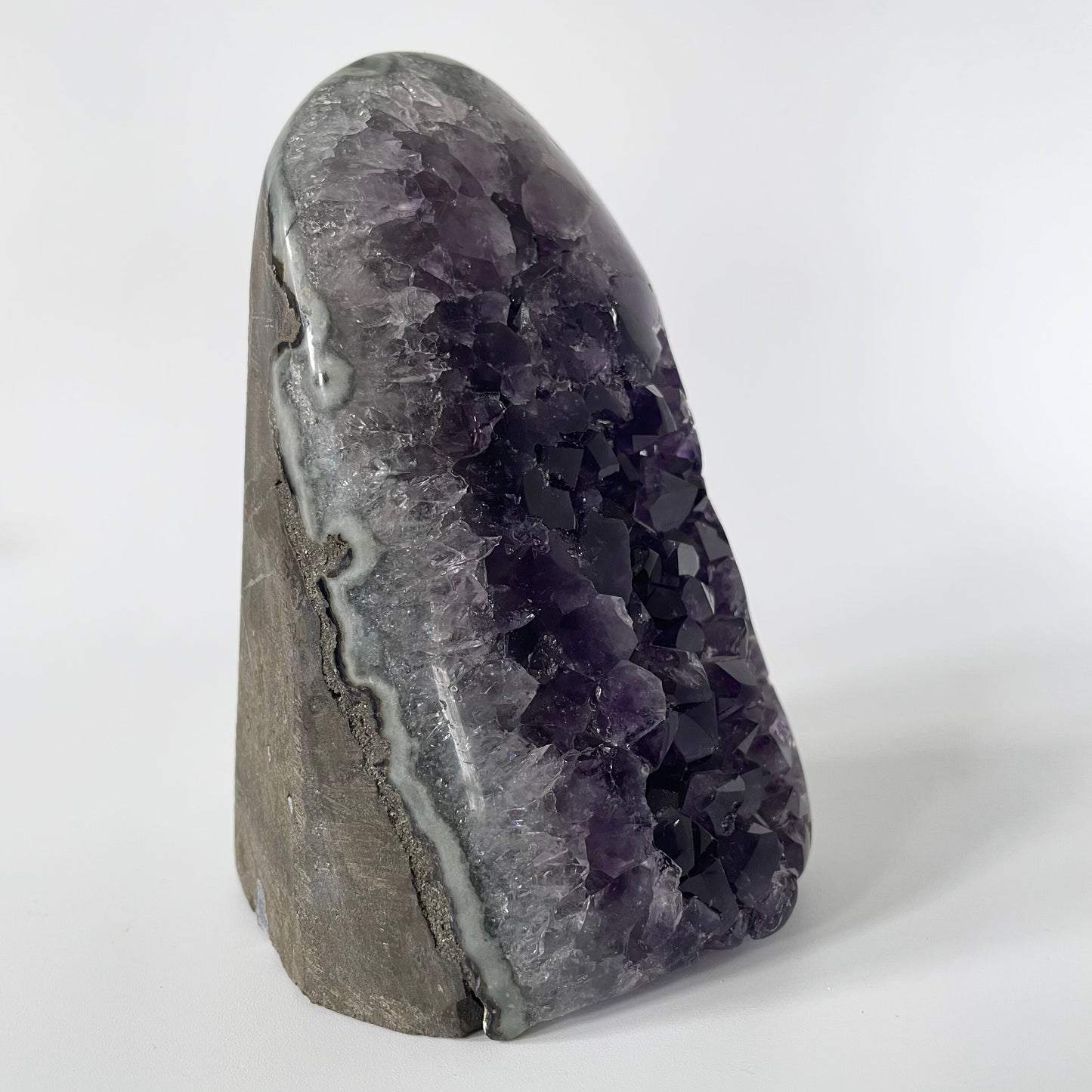 Amethyst cluster with polished edges and brilliant hues of deep purple and various sizes of crystal formations on a white background.