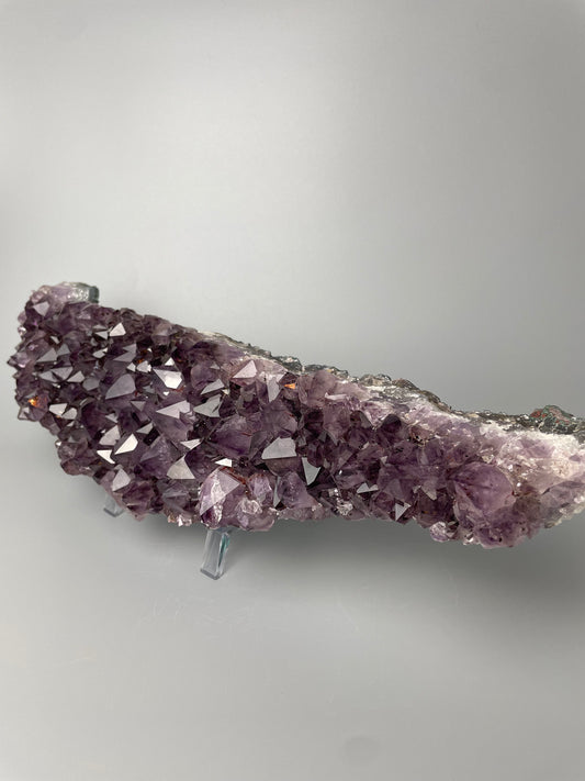 Amethyst cluster with brilliant hues of purple and various sizes of crystal formations on a gray background.