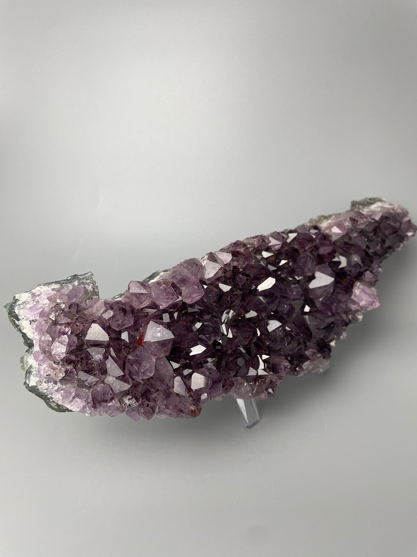 Amethyst cluster with brilliant hues of purple and various sizes of crystal formations on a gray background.