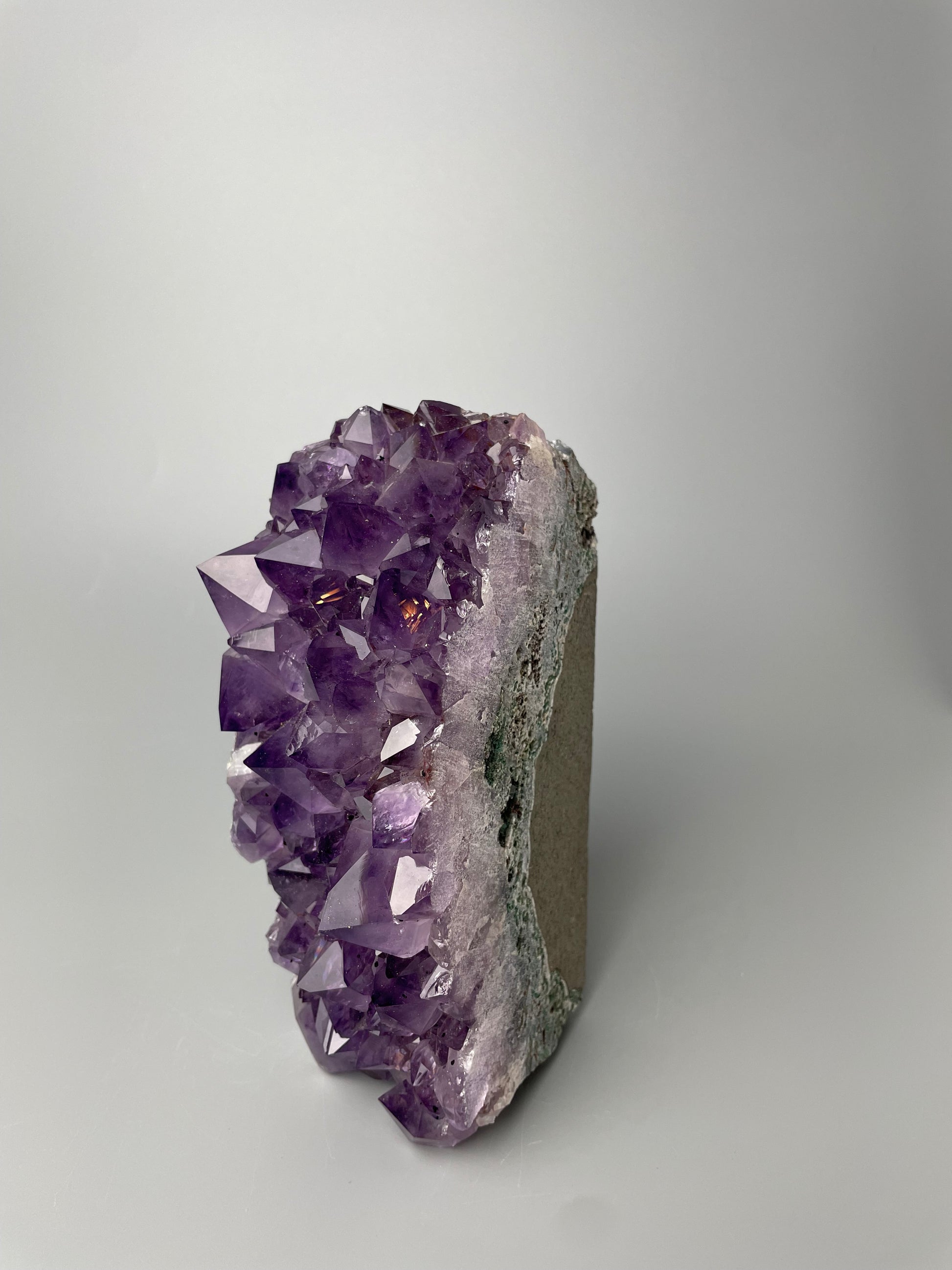 Amethyst cluster with brilliant hues of purple and various sizes of crystal formations on a gray background.