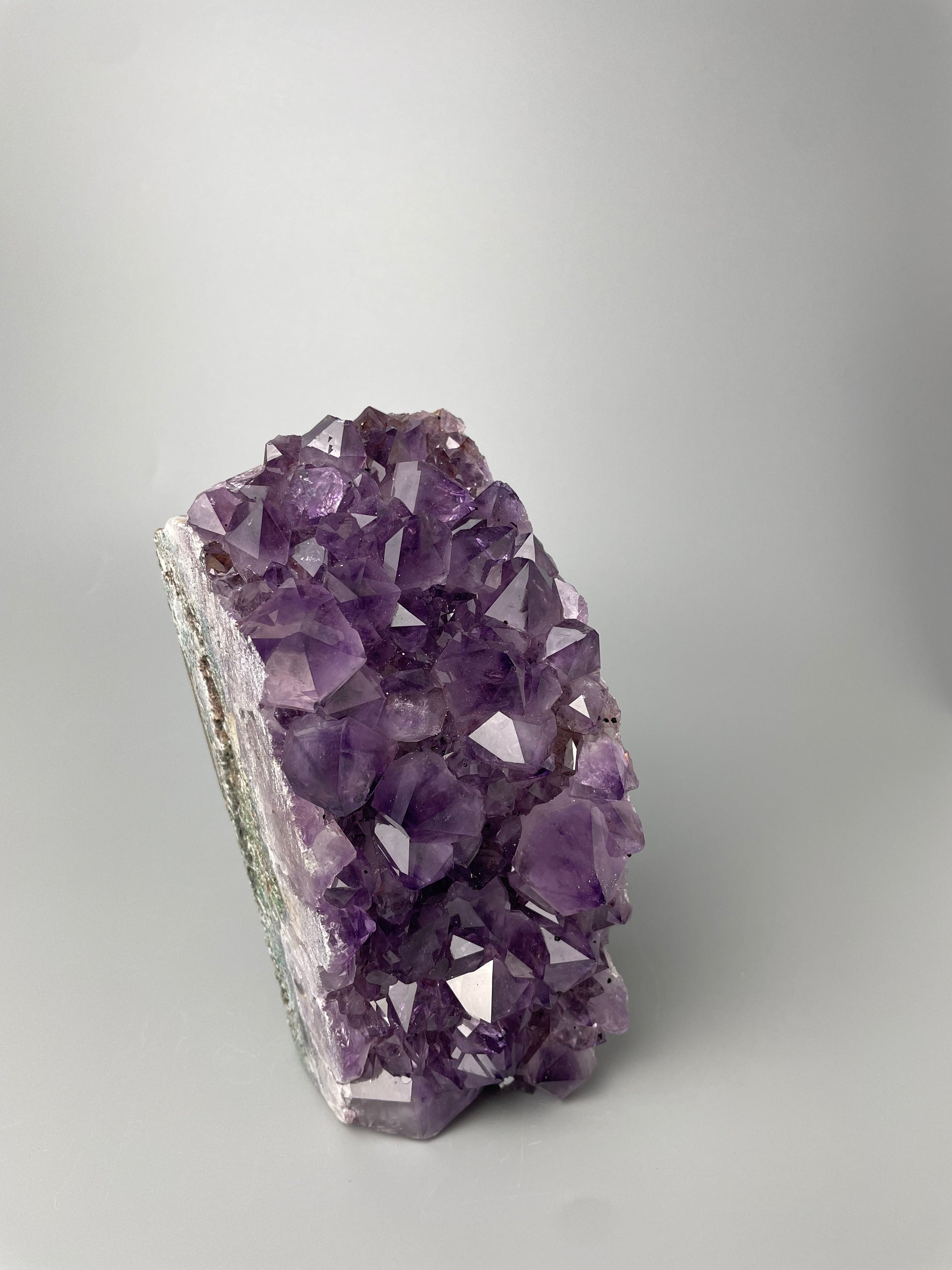 Amethyst cluster with brilliant hues of purple and various sizes of crystal formations on a gray background.