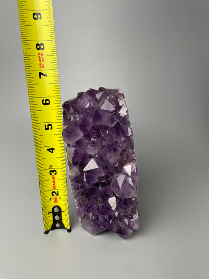 Amethyst cluster with brilliant hues of purple and various sizes of crystal formations on a gray background.