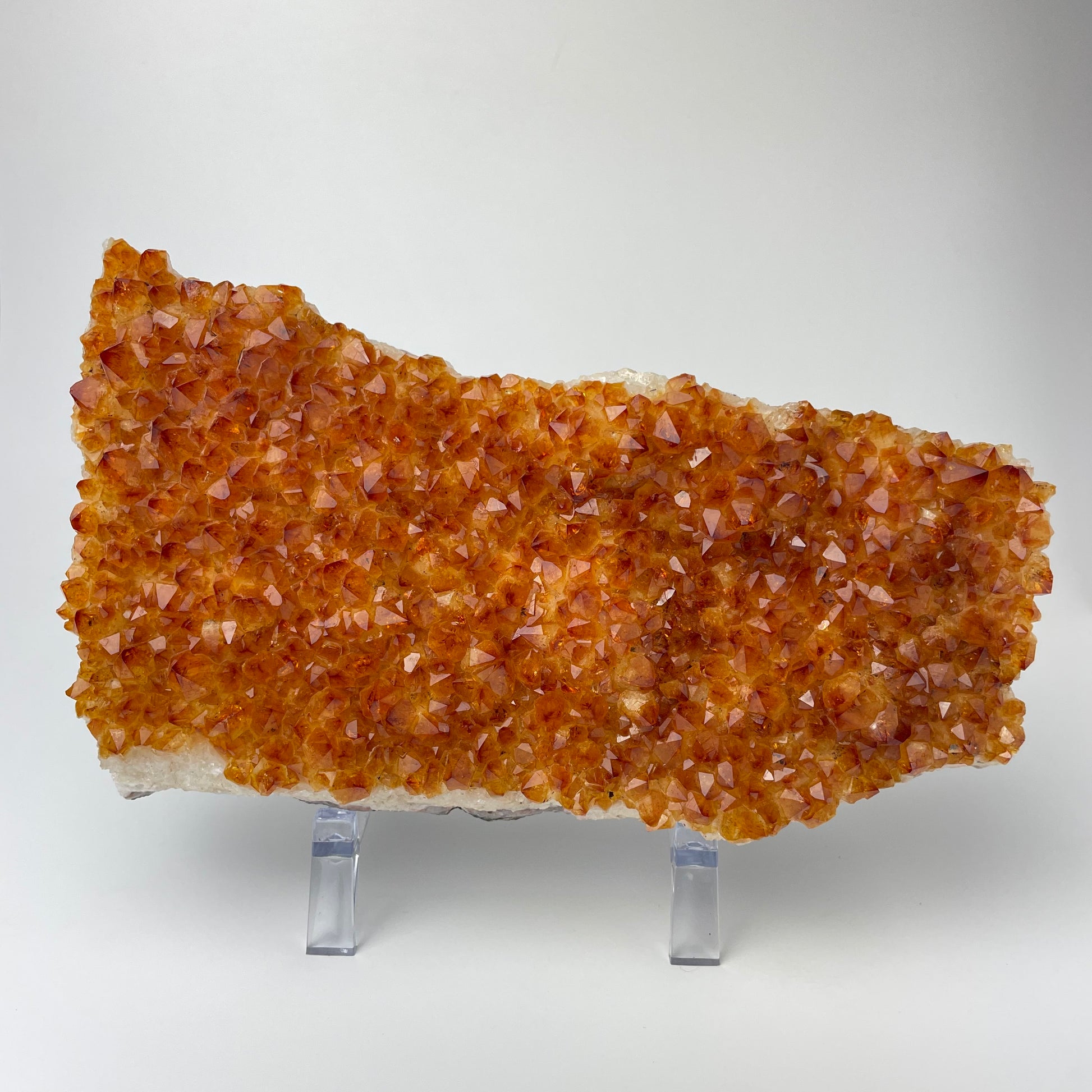 Citrine cluster with deep, orange-colored crystal formations on an acrylic stand against a gray background. 