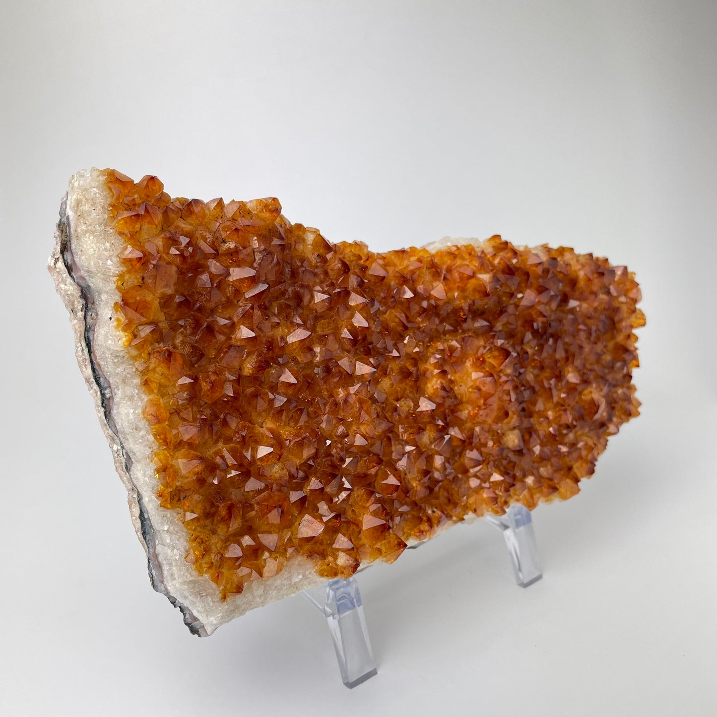 Citrine cluster with deep, orange-colored crystal formations on an acrylic stand against a gray background. 