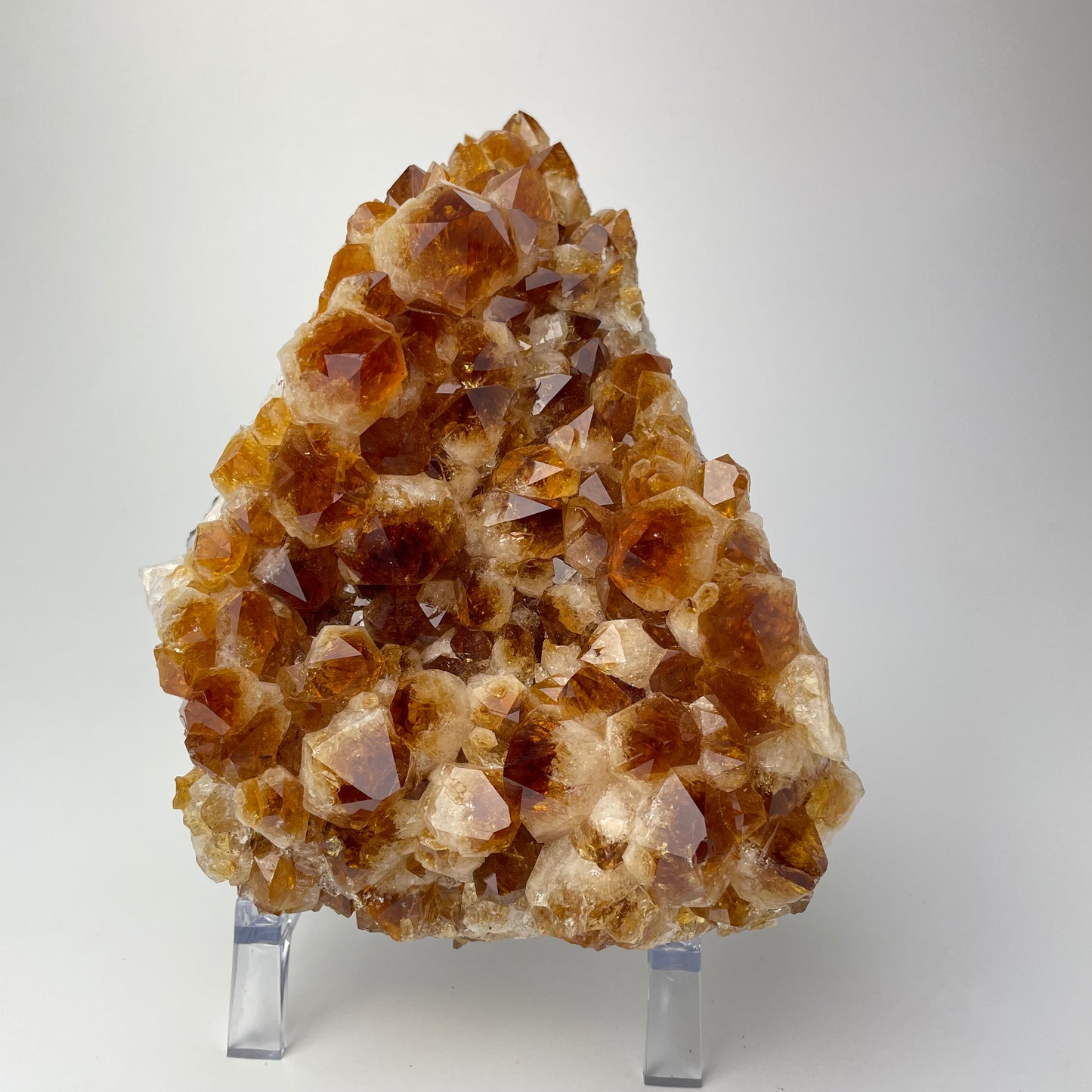 Citrine cluster with deep, orange-colored crystal formations on an acrylic stand against a gray background. 