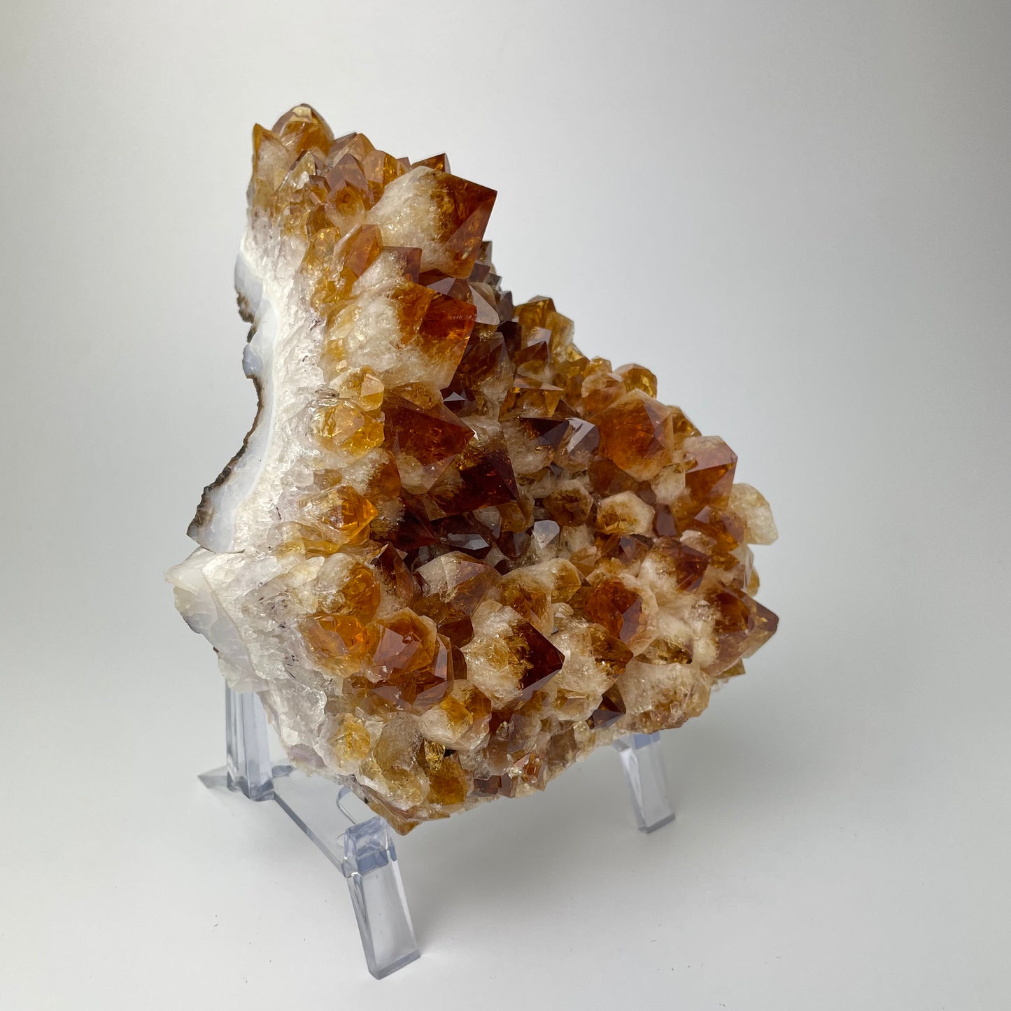 Citrine cluster with deep, orange-colored crystal formations on an acrylic stand against a gray background. 