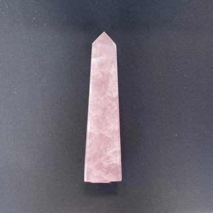 A polished rose quartz obelisk, approximately five inches in height, showcasing a soft pink hue with natural marbling and reflections of light.