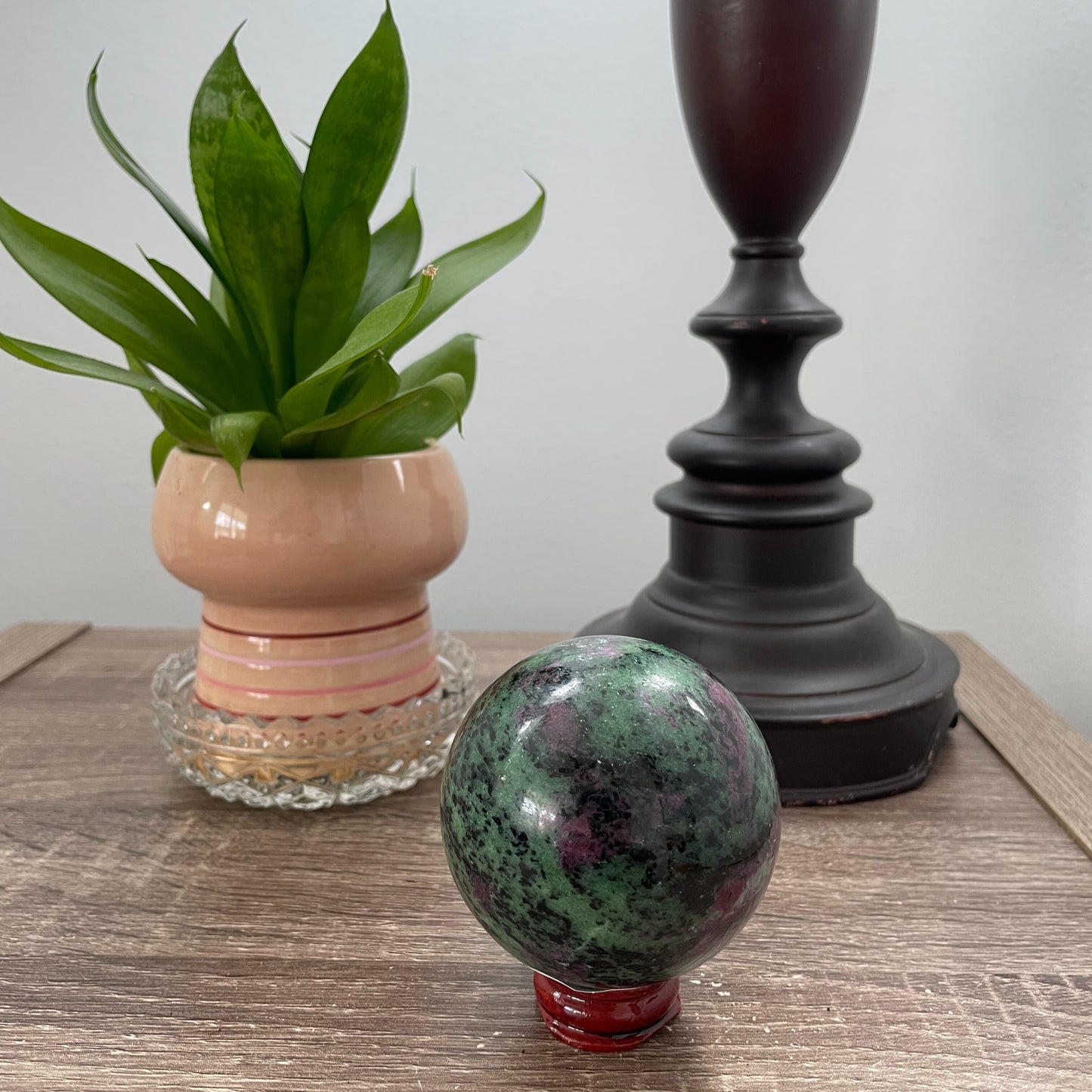 A close-up image of a vibrant ruby zoisite sphere, measuring nearly three inches in diameter. The sphere showcases a captivating blend of rich ruby red and deep green hues, with intricate patterns and veins running throughout its polished surface.