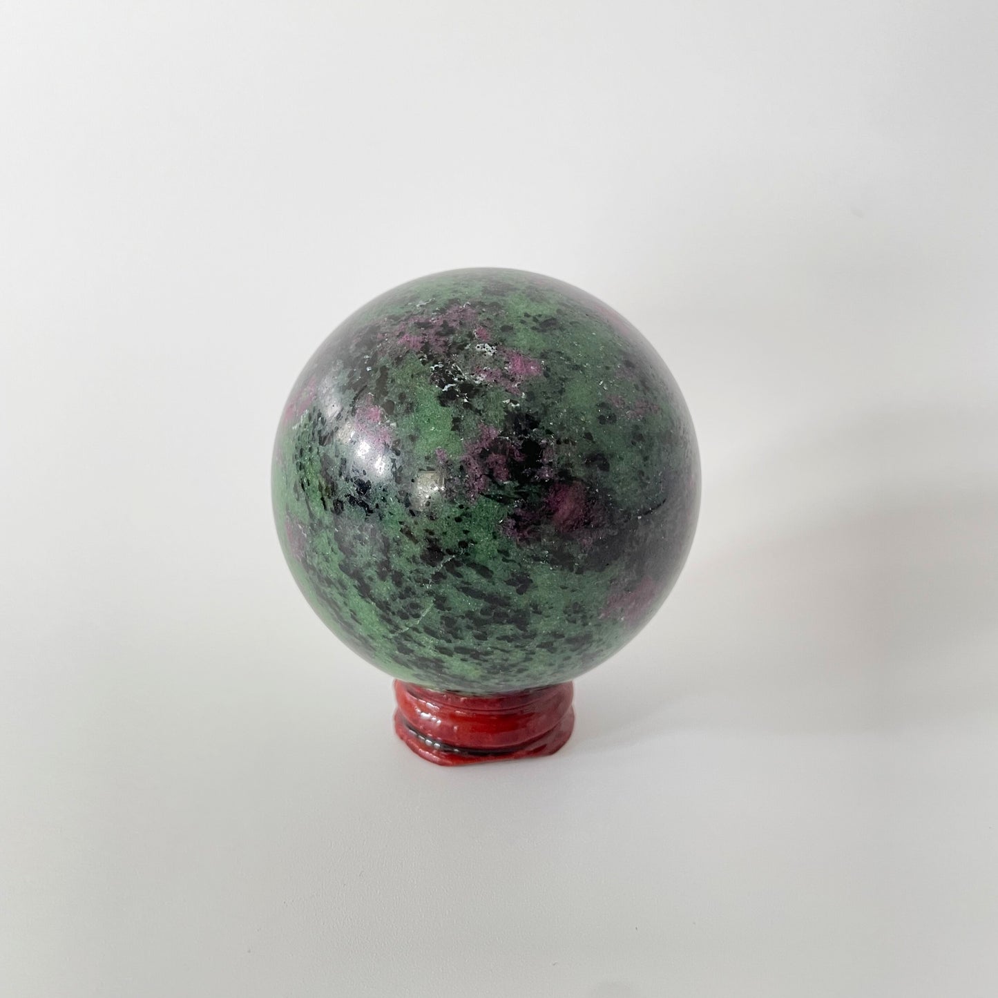 A close-up image of a vibrant ruby zoisite sphere, measuring nearly three inches in diameter. The sphere showcases a captivating blend of rich ruby red and deep green hues, with intricate patterns and veins running throughout its polished surface.