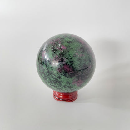 A close-up image of a vibrant ruby zoisite sphere, measuring nearly three inches in diameter. The sphere showcases a captivating blend of rich ruby red and deep green hues, with intricate patterns and veins running throughout its polished surface.