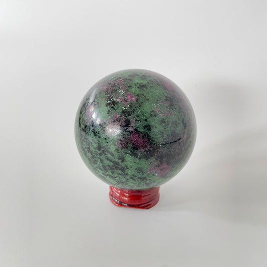 A close-up image of a vibrant ruby zoisite sphere, measuring nearly three inches in diameter. The sphere showcases a captivating blend of rich ruby red and deep green hues, with intricate patterns and veins running throughout its polished surface.