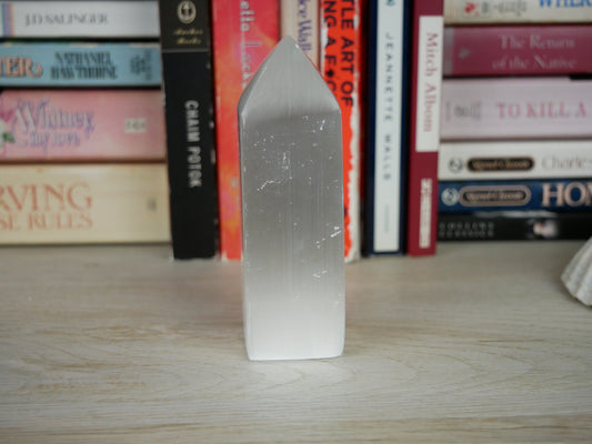 Close-up image of a 1.32-inch Selenite obelisk, showcasing its smooth, polished surface and translucent quality. The obelisk stands tall with a tapered, four-sided shape, emitting a soft glow as light passes through its crystalline structure.