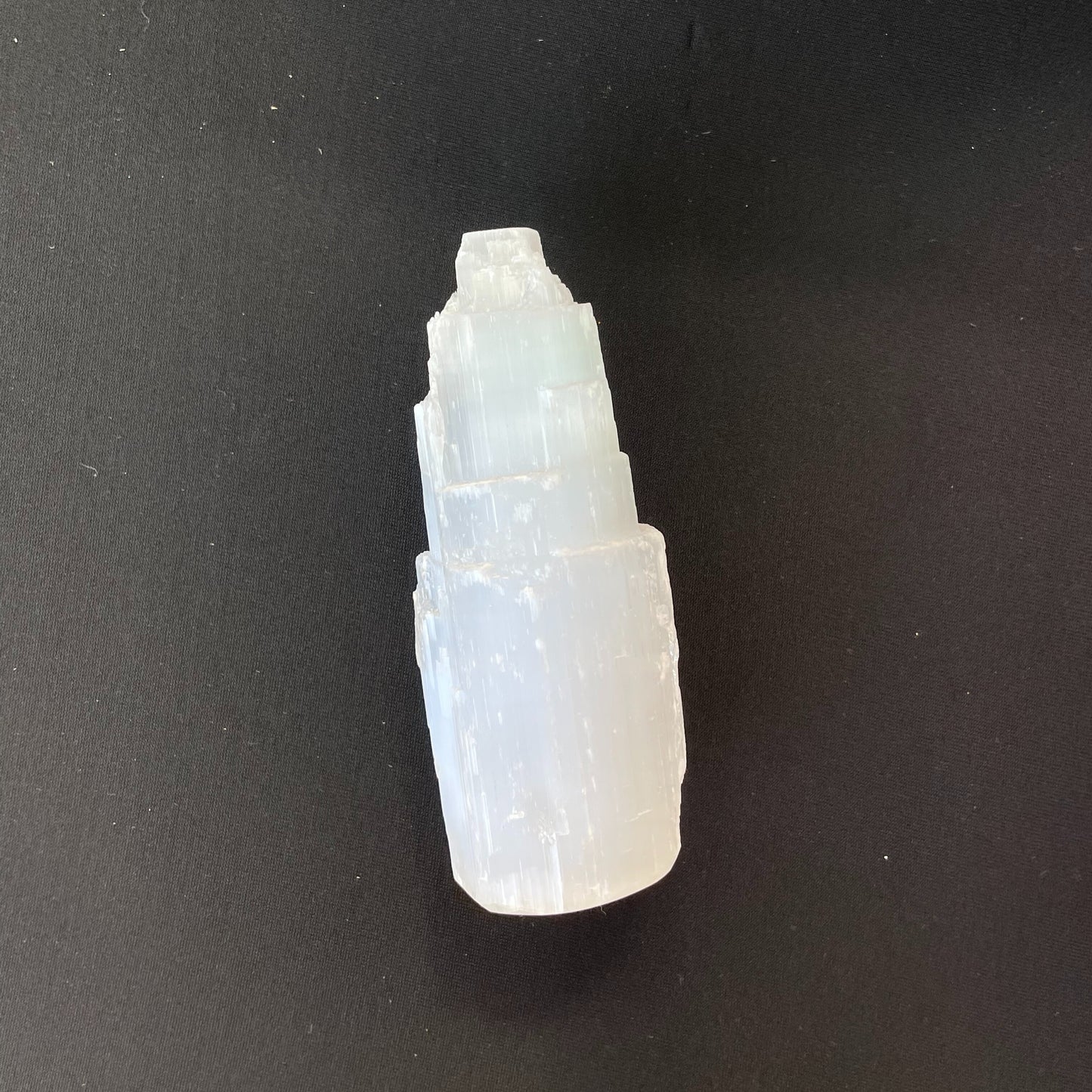 Close-up of a Selenite Tower, approximately two inches in height, showcasing its translucent, striated structure under soft lighting.