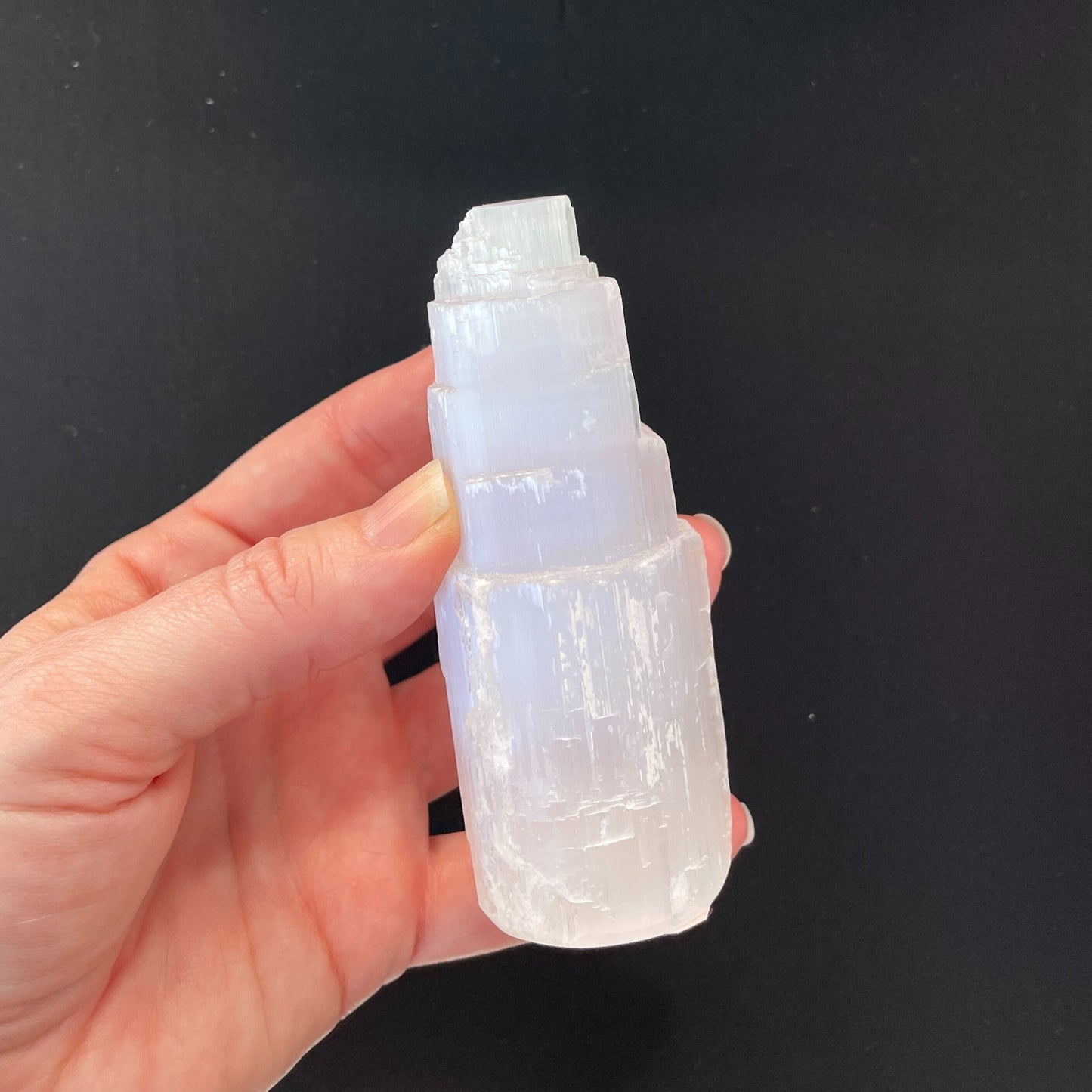 Close-up of a Selenite Tower, approximately two inches in height, showcasing its translucent, striated structure under soft lighting.