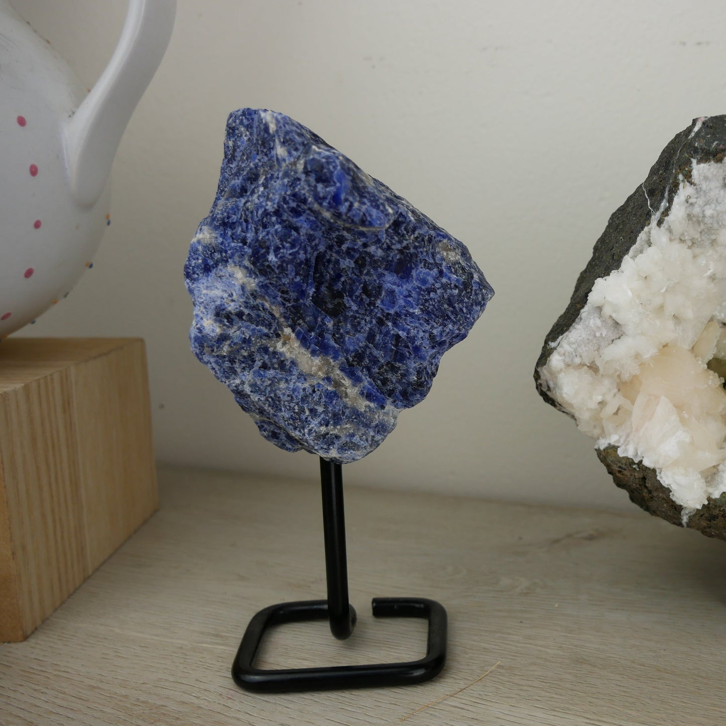 Close-up image of a vibrant blue sodalite mineral specimen, delicately perched on a sleek stand against a neutral background.