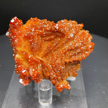 Close-up photo of 86.8 grams of stunning Vanadinite crystals sitting atop a bed of Barite. The vibrant red-orange Vanadinite crystals sparkle under the light, creating a mesmerizing display against the white Barite backdrop.