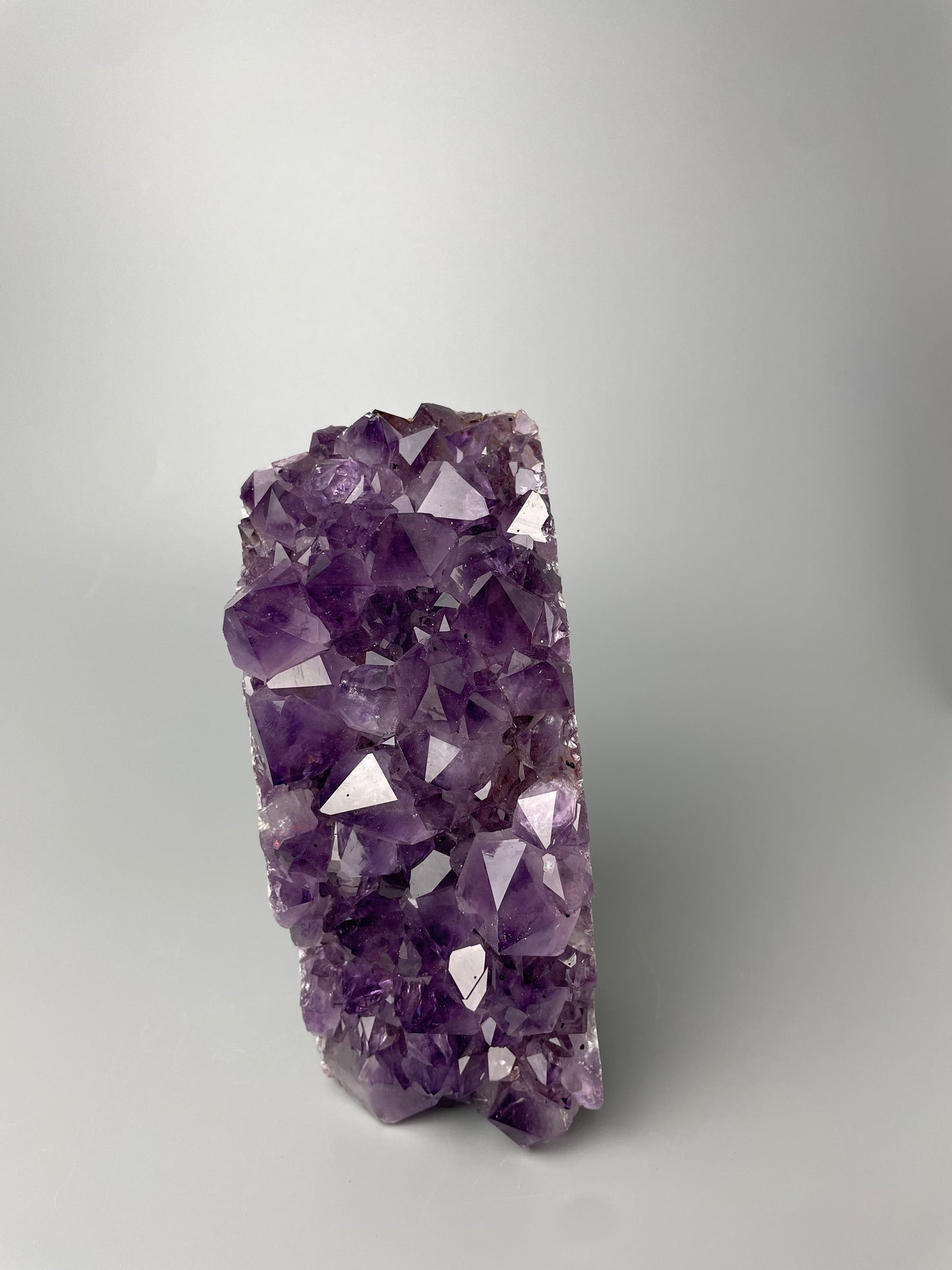 Amethyst cluster with brilliant hues of purple and various sizes of crystal formations on a gray background.