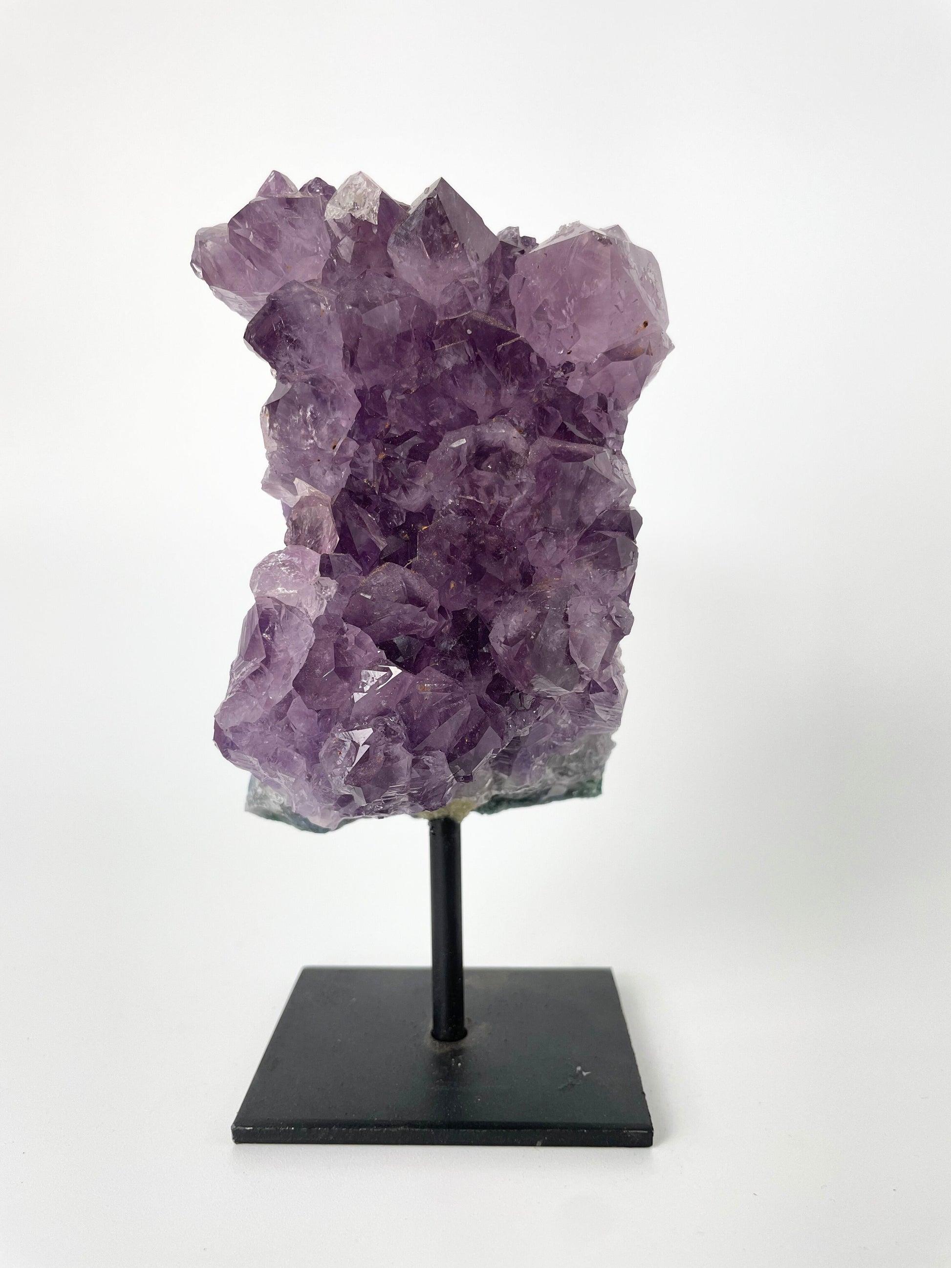 Image shows a stunning amethyst specimen resting on a sleek metal stand, showcasing its vibrant purple hues and intricate crystal formations.