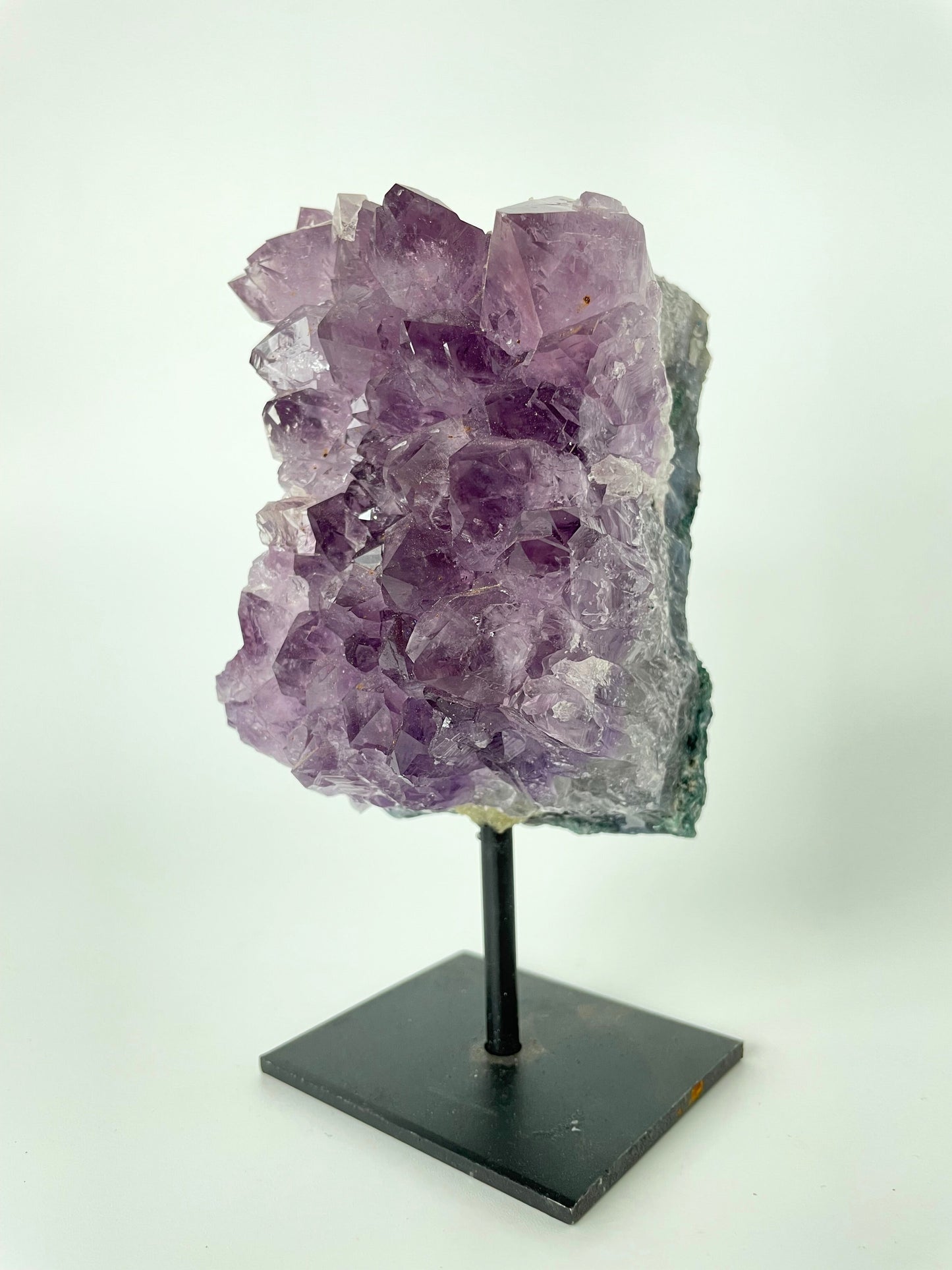 Image shows a stunning amethyst specimen resting on a sleek metal stand, showcasing its vibrant purple hues and intricate crystal formations.