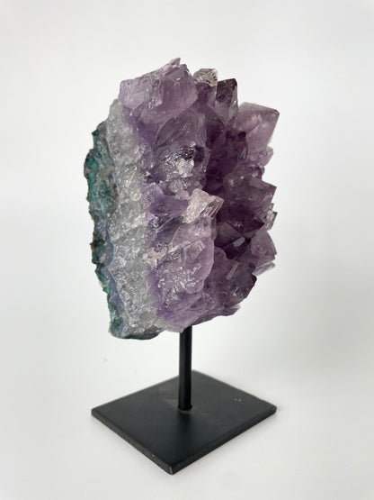 Image shows a stunning amethyst specimen resting on a sleek metal stand, showcasing its vibrant purple hues and intricate crystal formations.