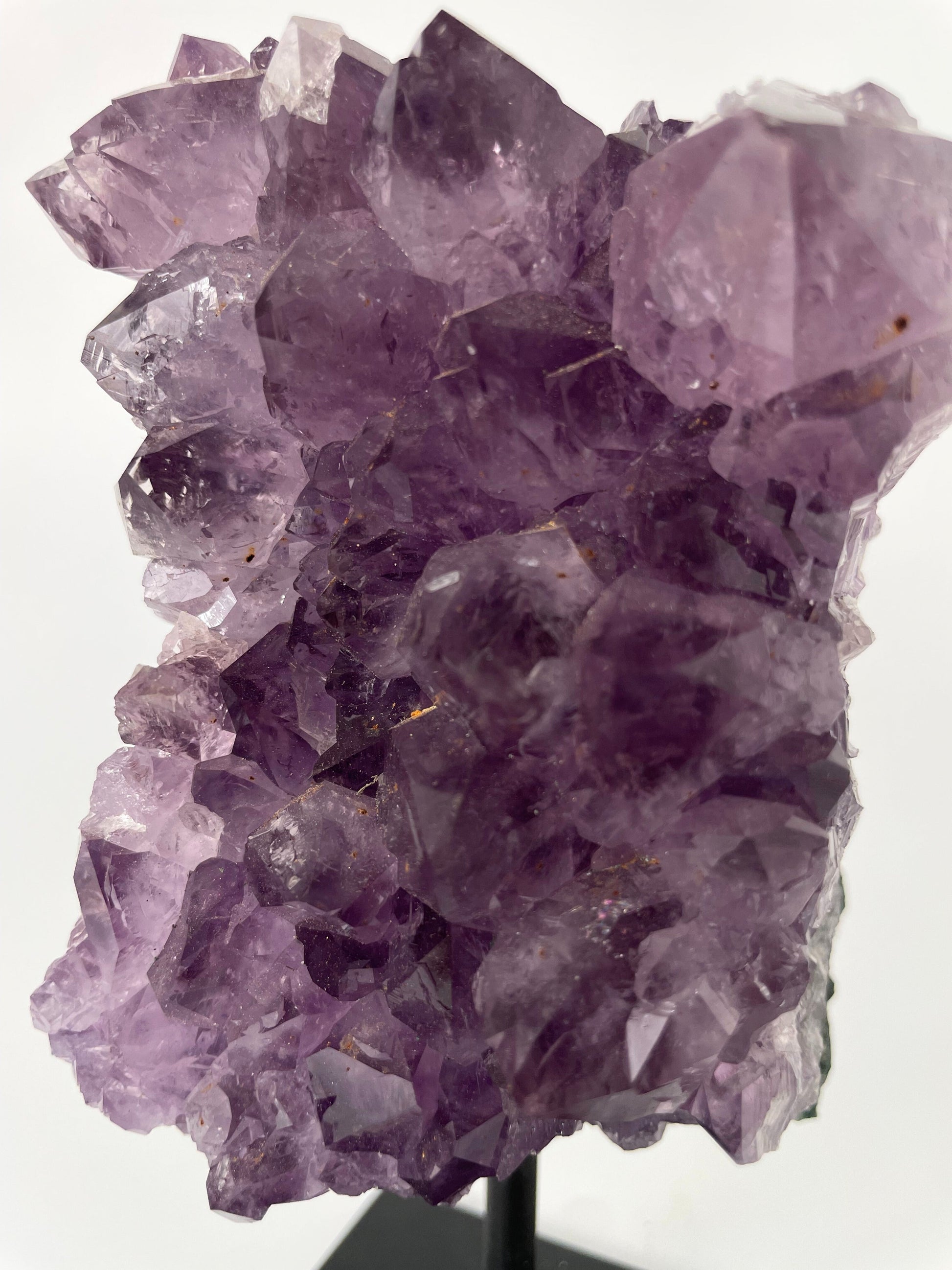 Image shows a stunning amethyst specimen resting on a sleek metal stand, showcasing its vibrant purple hues and intricate crystal formations.