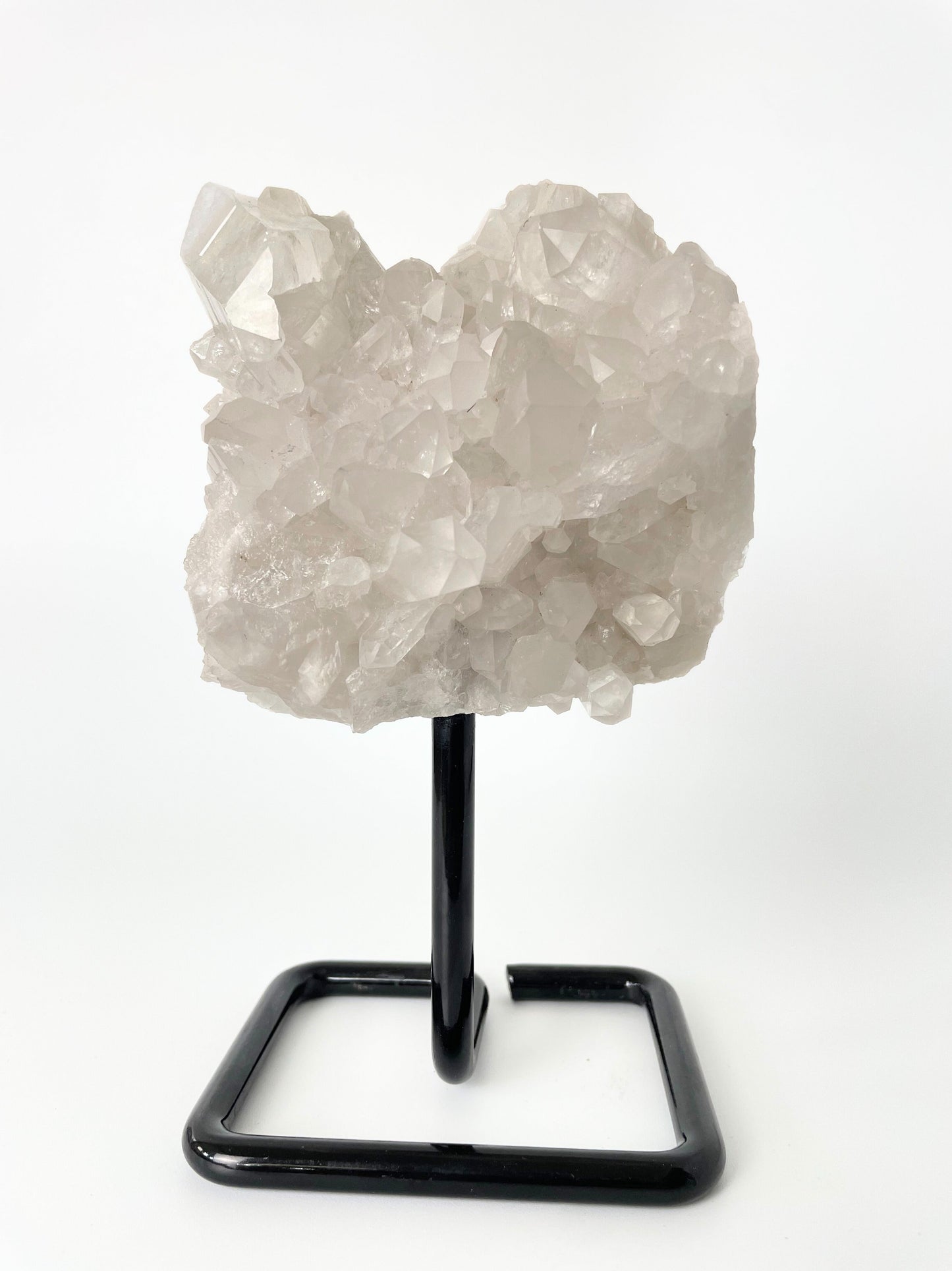 Clear quartz cluster resting elegantly on a sleek metal stand, showcasing the crystal's pristine beauty and natural allure.