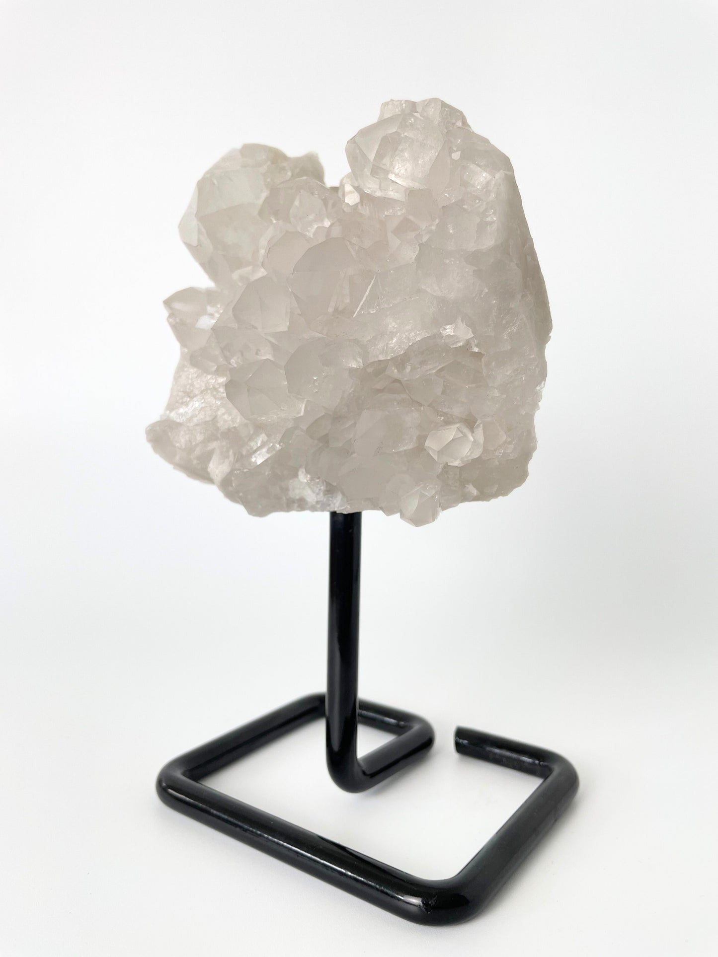 Clear quartz cluster resting elegantly on a sleek metal stand, showcasing the crystal's pristine beauty and natural allure.