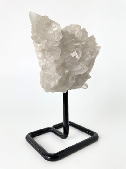 Clear quartz cluster resting elegantly on a sleek metal stand, showcasing the crystal's pristine beauty and natural allure.