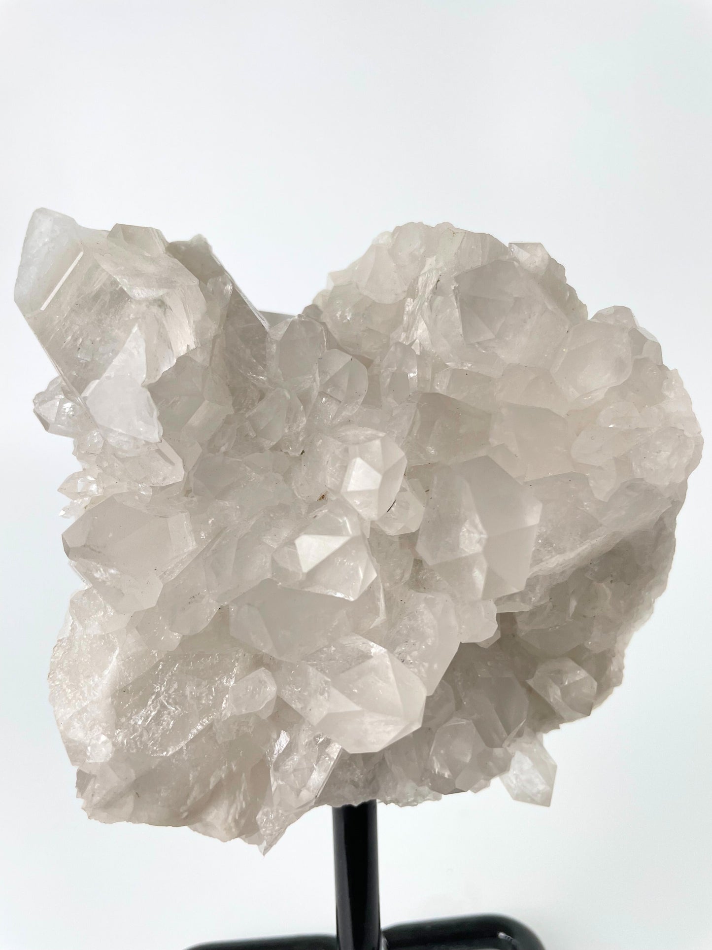 Clear quartz cluster resting elegantly on a sleek metal stand, showcasing the crystal's pristine beauty and natural allure.