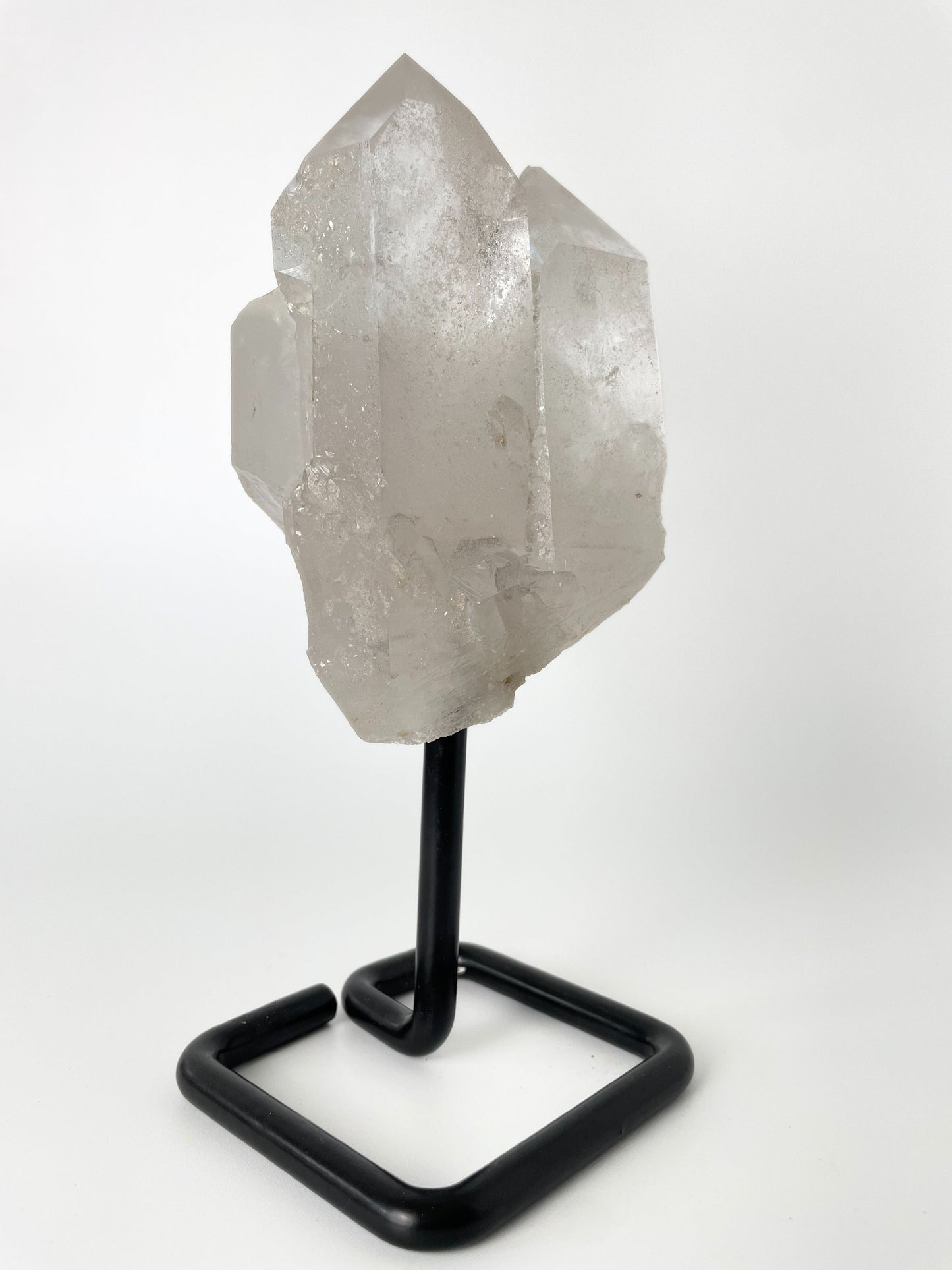 Clear quartz cluster resting elegantly on a sleek metal stand, showcasing the crystal's pristine beauty and natural allure.